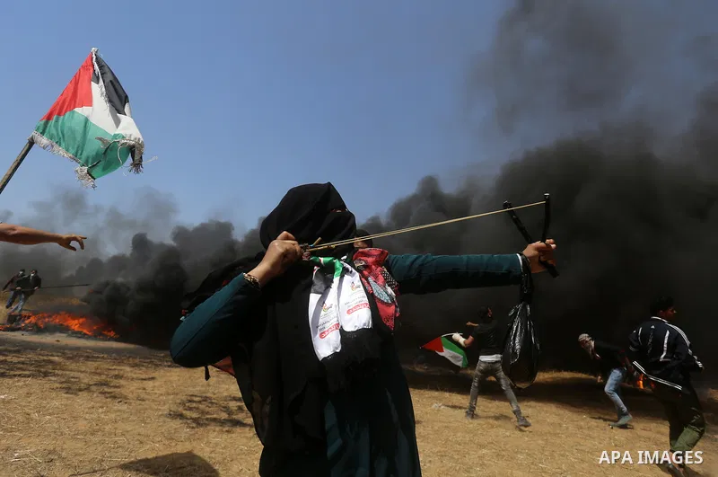 A Palestinian woman uses a slingshot to hurl stones towards Israeli security forces during clashes at the Israel-Gaza border in a tent city protest demanding the right to return to their homeland, in Khan Younis in the s...