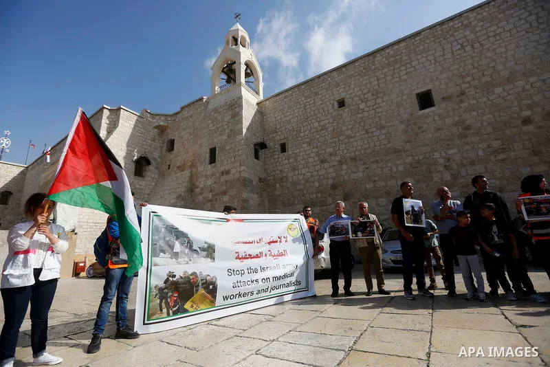 Palestinian medicals hold placards during a protest demanding to stop Israeli attacks on paramedics and journalists outside Church of the Nativity in the West Bank city of Bethlehem, on April 8, 2018. Photo by Wisam Hash...