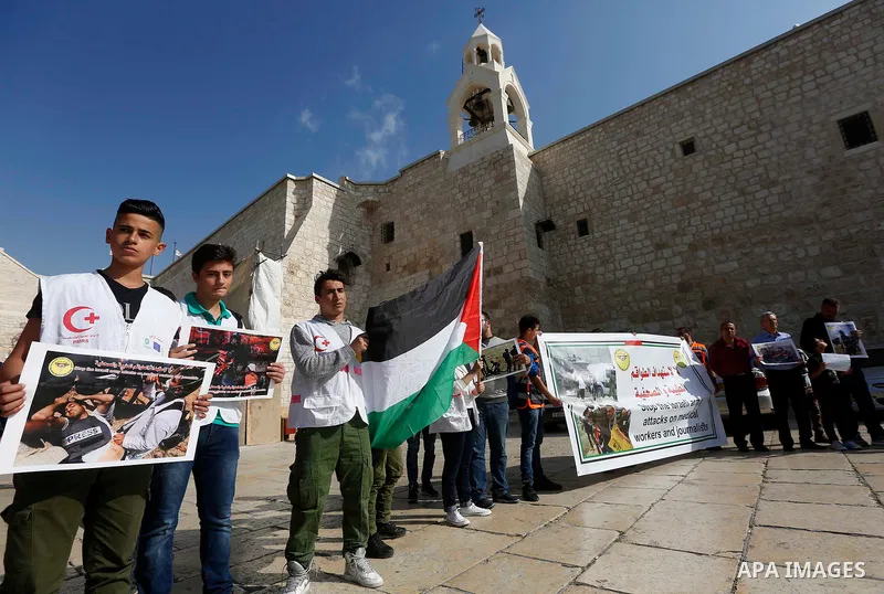 Palestinian medicals hold placards during a protest demanding to stop Israeli attacks on paramedics and journalists outside Church of the Nativity in the West Bank city of Bethlehem, on April 8, 2018. Photo by Wisam Hash...
