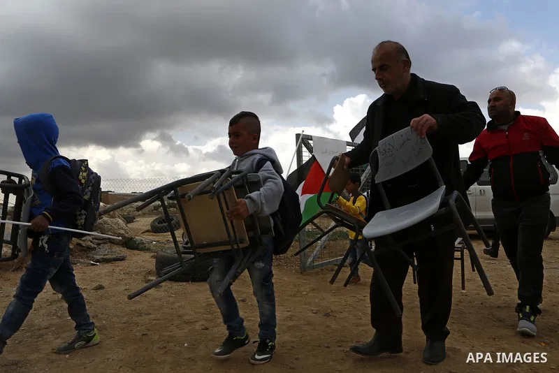 Palestinian schoolboys carry chairs at the site of their school after Israeli forces it was demolished by Israeli security forces who claim it was built on illegal land, in the West Bank city of Hebron on April 10, 2018....