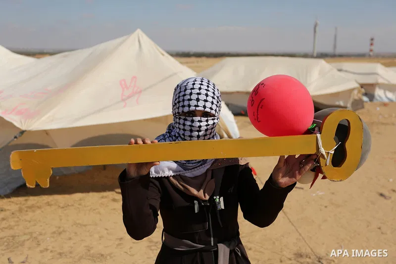 A Palestinian woman holds symbolic key and balloons during a protest demanding the right to return to their homeland, at the Israel-Gaza border, in Rafah in the southern Gaza Strip on April 10, 2018. Photo by Ashraf Amra