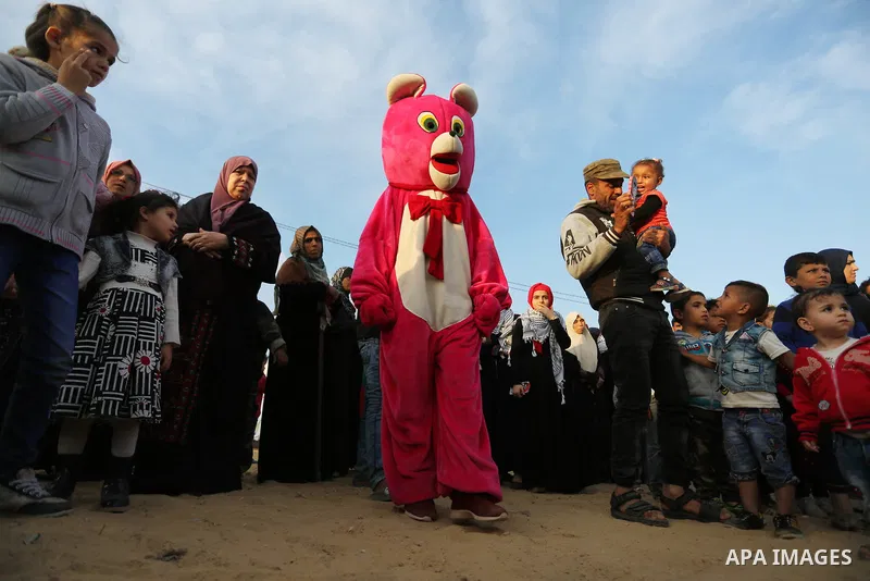 A Palestinian man wearing costume is seen near tents during a tent city protest demanding the right to return to their homeland, at the Israel-Gaza border in the east of Gaza city on April 11, 2018. Photo by Ashraf Amra