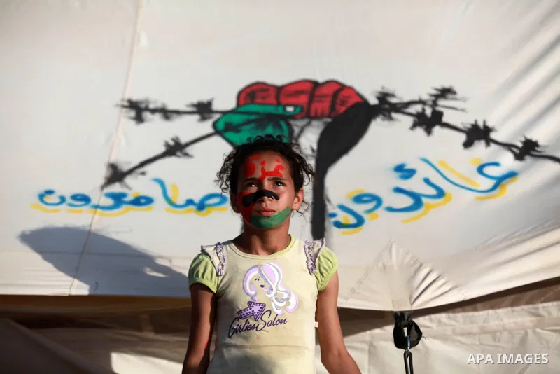 A Palestinian girl with written on her face "Gaza" stands next to a tent during a tent city protest demanding the right to return to their homeland, at the Israel-Gaza border in the east of Gaza city on April 11, 2018. P...