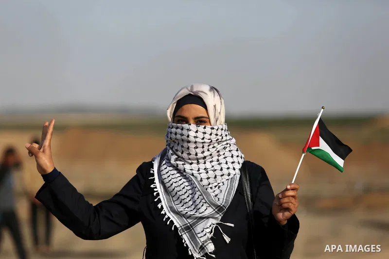 A Palestinian woman waves a Palestinian flag during a tent city protest demanding the right to return to their homeland, at the Israel-Gaza border in the east of Gaza city on April 11, 2018. Photo by Ashraf Amra