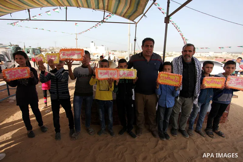 Palestinians show traditional sweets which was prepared during a tent city protest demanding the right to return to their homeland, at the Israel-Gaza border in the east of Gaza city on April 12, 2018. Photo by Mahmoud A...