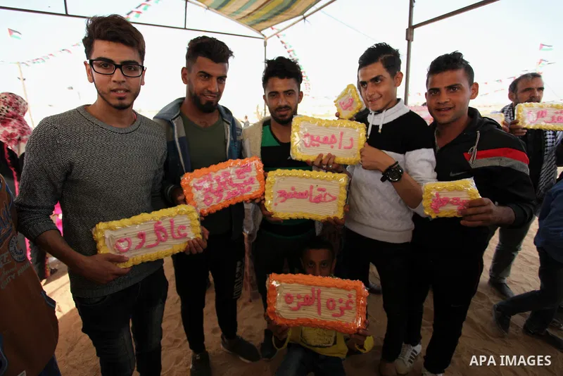 Palestinians show traditional sweets which was prepared during a tent city protest demanding the right to return to their homeland, at the Israel-Gaza border in the east of Gaza city on April 12, 2018. Photo by Mahmoud A...