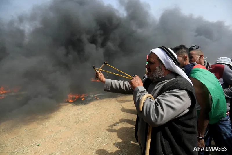 A Palestinian man uses a slingshot to hurl stones towards Israeli security forces during clashes in a tent city protest where Palestinians demand the right to return to their homeland, at the Israel-Gaza border, in Khan...