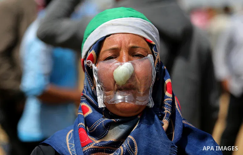 A picture taken on April 13, 2018, shows a Palestinian woman covers her face to protect herself from tear gas during clashes with Israeli security forces following a protest, on the Gaza-Israel border, in Khan Younis in...