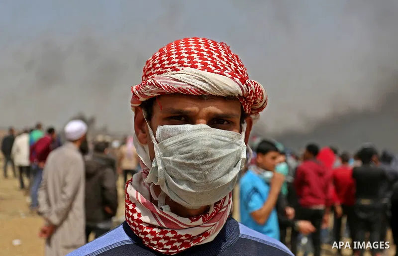 A picture taken on April 13, 2018, shows a Palestinian protester covers his face to protect himself from tear gas during clashes with Israeli security forces following a protest, on the Gaza-Israel border, in Khan Younis...