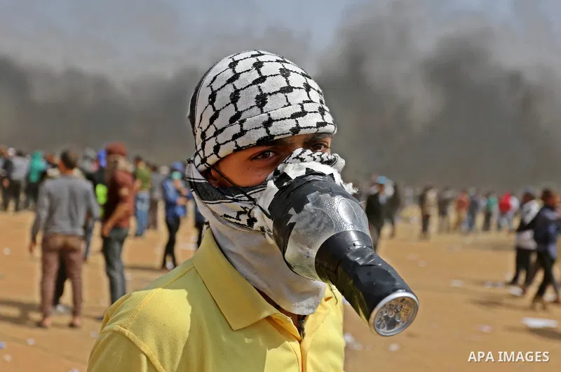 A picture taken on April 13, 2018, shows a Palestinian protester covers his face to protect himself from tear gas during clashes with Israeli security forces following a protest, on the Gaza-Israel border, in Khan Younis...