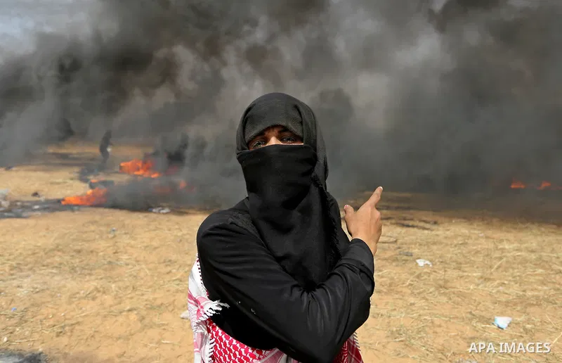 A picture taken on April 13, 2018, shows a Palestinian woman covers her face to protect herself from tear gas during clashes with Israeli security forces following a protest, on the Gaza-Israel border, in Khan Younis in...