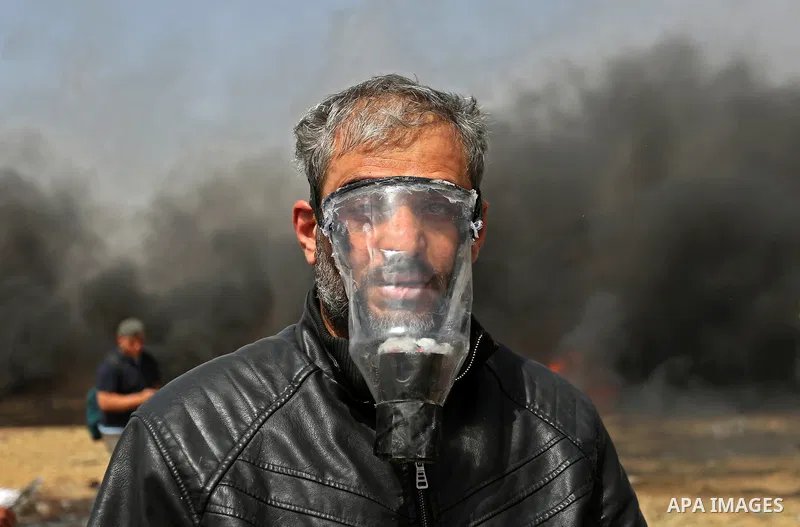 A picture taken on April 13, 2018, shows a Palestinian protester covers his face to protect himself from tear gas during clashes with Israeli security forces following a protest, on the Gaza-Israel border, in Khan Younis...