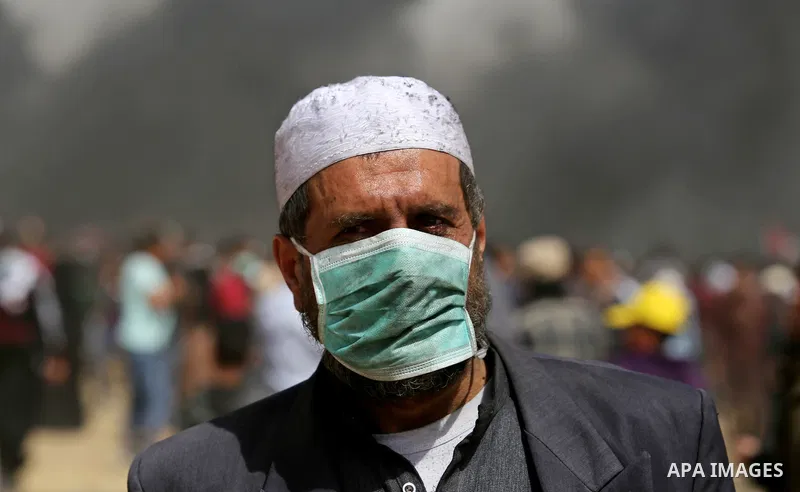 A picture taken on April 13, 2018, shows a Palestinian protester covers his face to protect himself from tear gas during clashes with Israeli security forces following a protest, on the Gaza-Israel border, in Khan Younis...