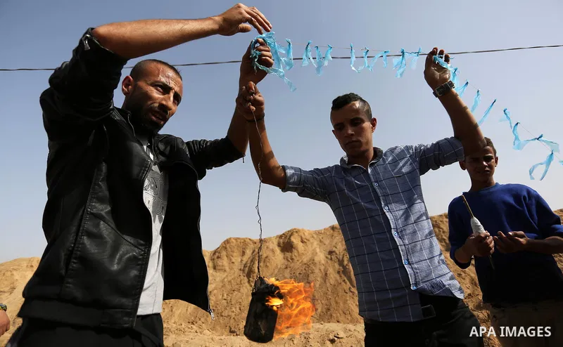 Palestinian youths attempt to tie a molotov cocktail with a string to a kite before trying to fly it over the border fence with Israel, in al-Bureij in the center of Gaza Strip on April 18, 2018. Photo by Ashraf Amra