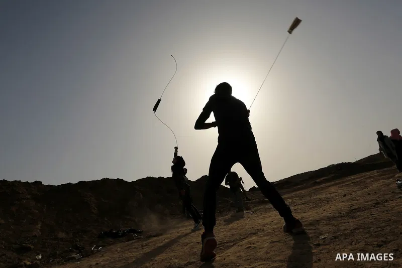 A Palestinian girl uses a slingshot to hurl stones towards Israeli security forces during clashes on the border between Israel and the Gaza Strip, in al-Bureij in the center of Gaza Strip on April 18, 2018. Photo by Ashr...