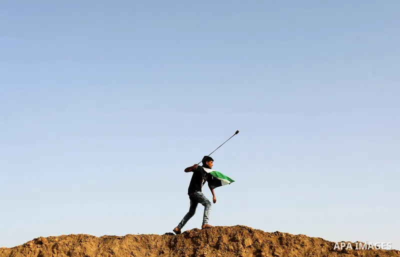 Palestinian protesters hurl stones towards Israeli security forces during clashes on the border between Israel and the Gaza Strip, in al-Bureij in the center of Gaza Strip on April 18, 2018. Photo by Ashraf Amra