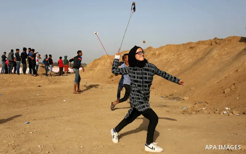 A Palestinian girl uses a slingshot to hurl stones towards Israeli security forces during clashes on the border between Israel and the Gaza Strip, in al-Bureij in the center of Gaza Strip on April 18, 2018. Photo by Ashr...