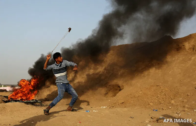 Palestinian protesters hurl stones towards Israeli security forces during clashes on the border between Israel and the Gaza Strip, in al-Bureij in the center of Gaza Strip on April 18, 2018. Photo by Ashraf Amra