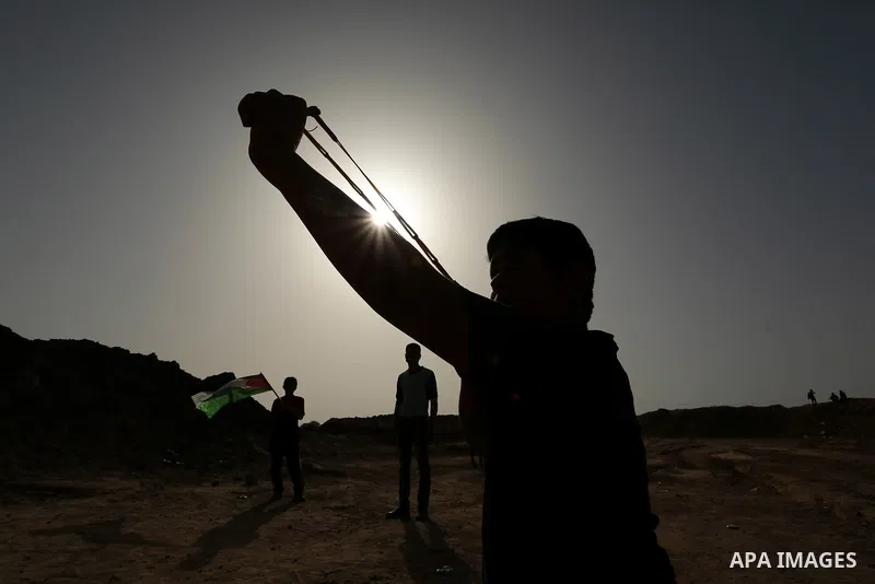 Palestinian protesters hurl stones towards Israeli security forces during clashes on the border between Israel and the Gaza Strip, in al-Bureij in the center of Gaza Strip on April 18, 2018. Photo by Ashraf Amra