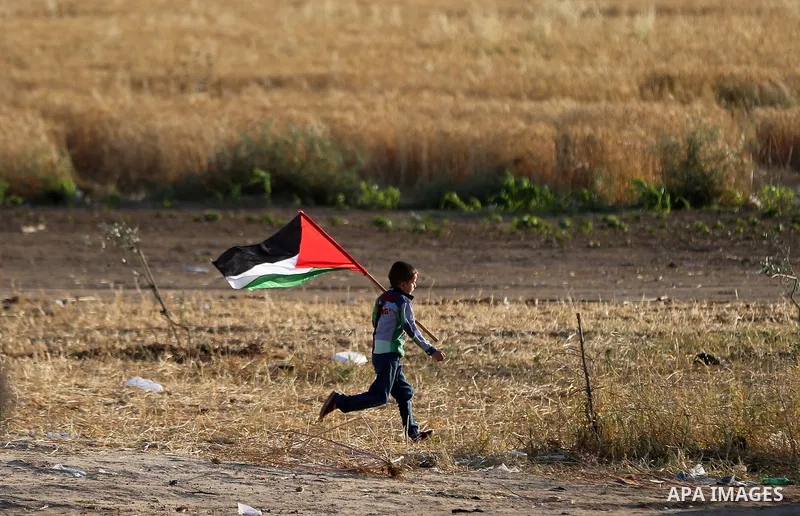 A Palestinian boy waves the national flag during tents protest demanding the right to return to their homeland, at the Israel-Gaza border in the east of Gaza city on April 23, 2018. Photo by Yasser Qudih