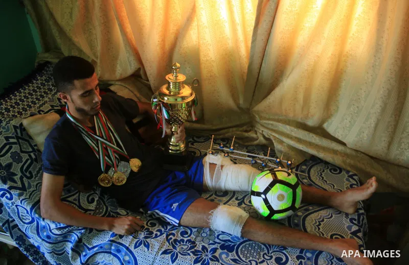 Palestinian football player Mohammed Abu Obaid, 26, who was shot in the leg by Israeli security forces during clashes in tents protest demanding the right to return to their homeland, at the Israel-Gaza border, lies on b...