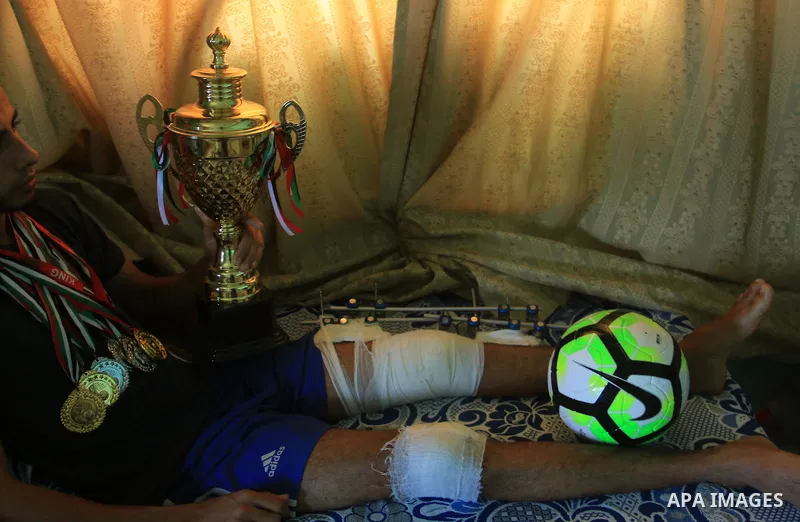 Palestinian football player Mohammed Abu Obaid, 26, who was shot in the leg by Israeli security forces during clashes in tents protest demanding the right to return to their homeland, at the Israel-Gaza border, lies on b...