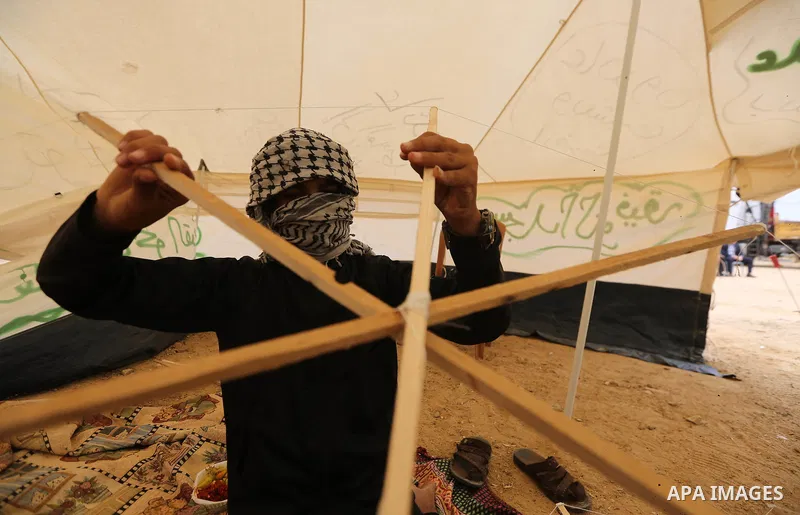 A masked Palestinian man prepares a kite to laden it with a molotov cocktail to use it during clashes with Israeli security forces at tents protest where Palestinians demand the right to return to their homeland, in east...