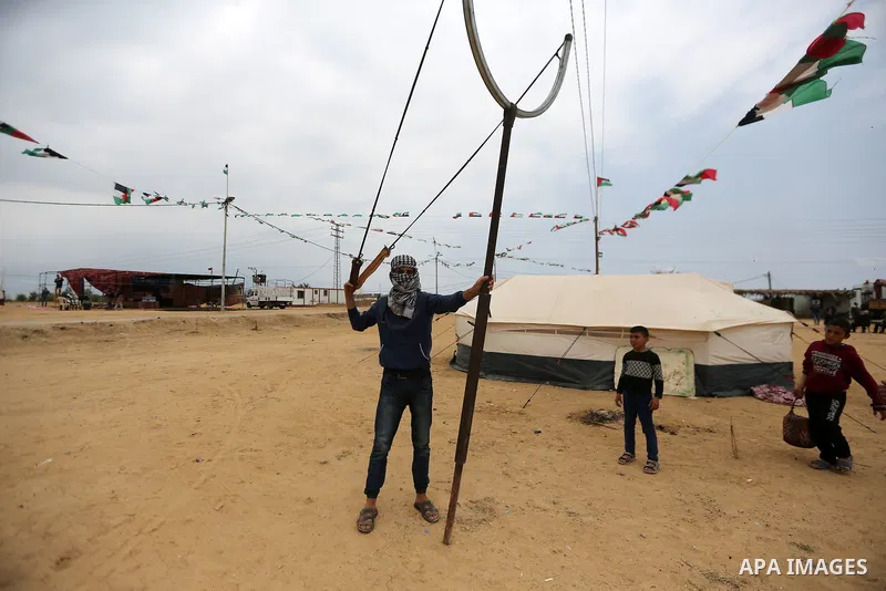 A masked Palestinian man holds a large slingshot to use it during clashes with Israeli security forces at tents protest where Palestinians demand the right to return to their homeland, in east of Gaza city on April 25, 2...
