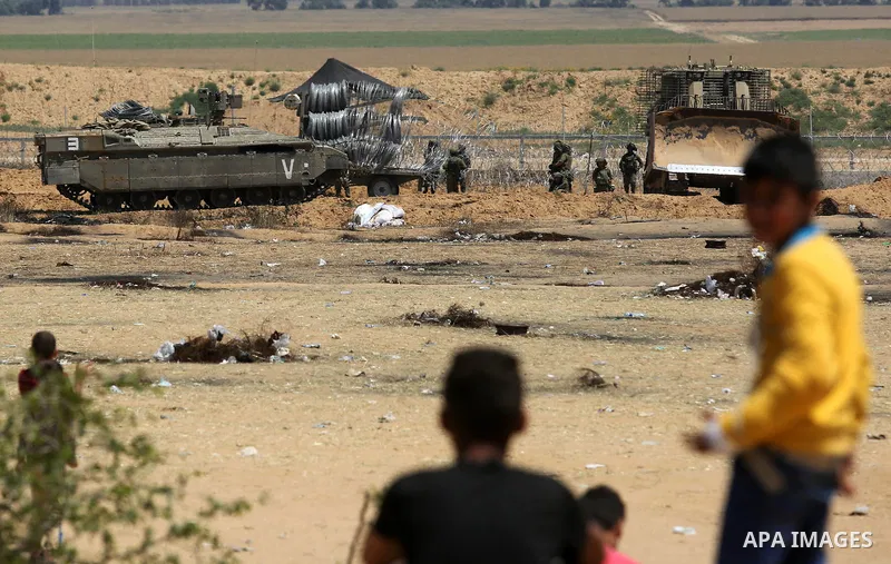 Palestinian youths look on as Israeli military machines work on the border between Israel and the Gaza Strip, in Khan Younis in the southern Gaza Strip on April 29, 2018. Photo by Ashraf Amra