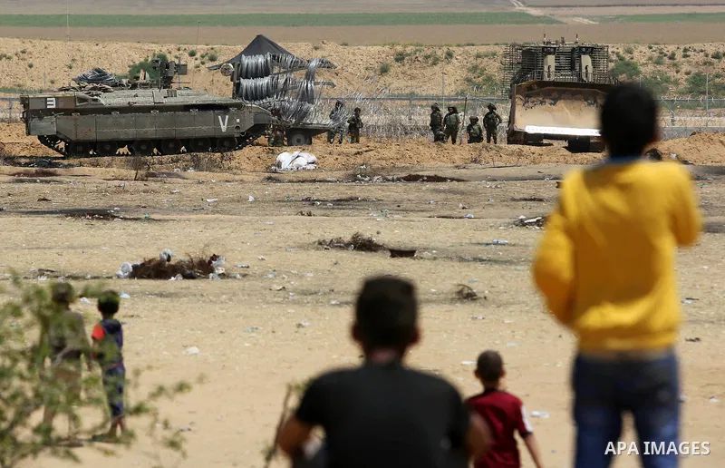 Palestinian youths look on as Israeli military machines work on the border between Israel and the Gaza Strip, in Khan Younis in the southern Gaza Strip on April 29, 2018. Photo by Ashraf Amra