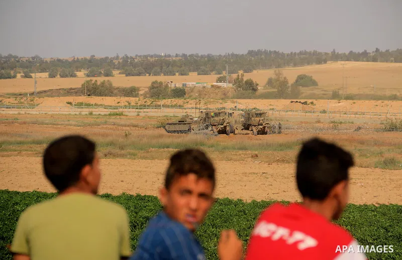 Palestinians look on as Israeli military machines work on the border between Israel and the Gaza Strip, in al-Bureij in the center of Gaza Strip on May 8, 2018. Photo by Mahmoud Khattab
