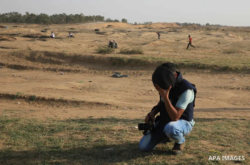 A Palestinian photographer takes cover during clashes with Israeli security froces in a tent city protest where Palestinians demand the right to return to their homeland and against U.S. embassy move to Jerusalem at the...