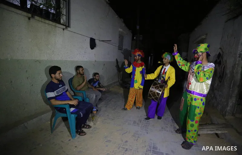 Palestinians dressed as clowns dawn awakener or Al Musaharati in Arabic, beat on their drums to wake Muslims for their overnight 'sahur', last meal, before the day's fast, as they walk through streets, in Dair Al Balah i...