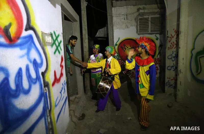 Palestinians dressed as clowns dawn awakener or Al Musaharati in Arabic, beat on their drums to wake Muslims for their overnight 'sahur', last meal, before the day's fast, as they walk through streets, in Dair Al Balah i...