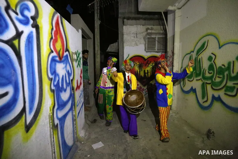 Palestinians dressed as clowns dawn awakener or Al Musaharati in Arabic, beat on their drums to wake Muslims for their overnight 'sahur', last meal, before the day's fast, as they walk through streets, in Dair Al Balah i...