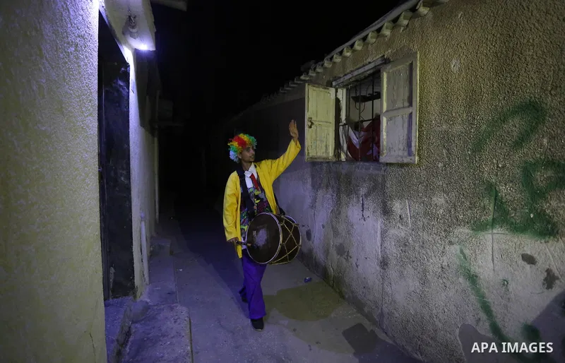 Palestinians dressed as clowns dawn awakener or Al Musaharati in Arabic, beat on their drums to wake Muslims for their overnight 'sahur', last meal, before the day's fast, as they walk through streets, in Dair Al Balah i...