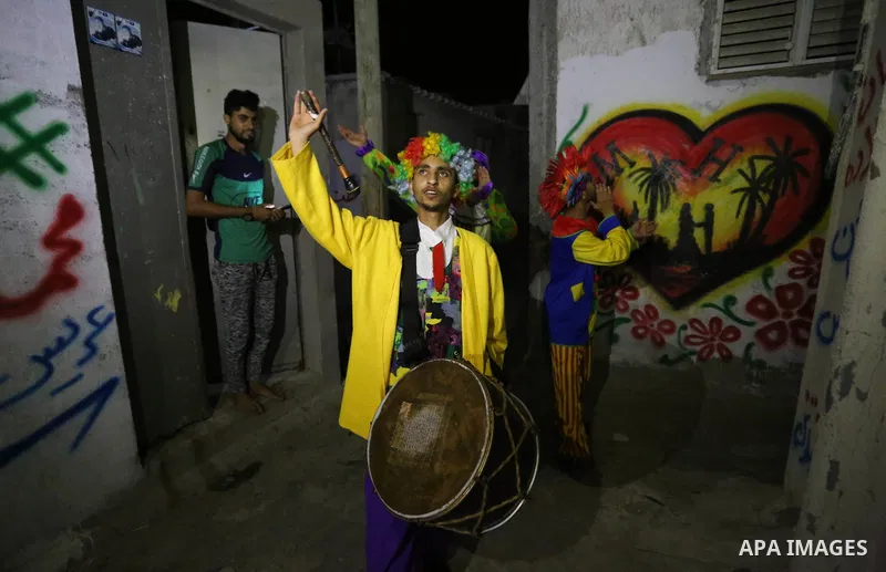 Palestinians dressed as clowns dawn awakener or Al Musaharati in Arabic, beat on their drums to wake Muslims for their overnight 'sahur', last meal, before the day's fast, as they walk through streets, in Dair Al Balah i...