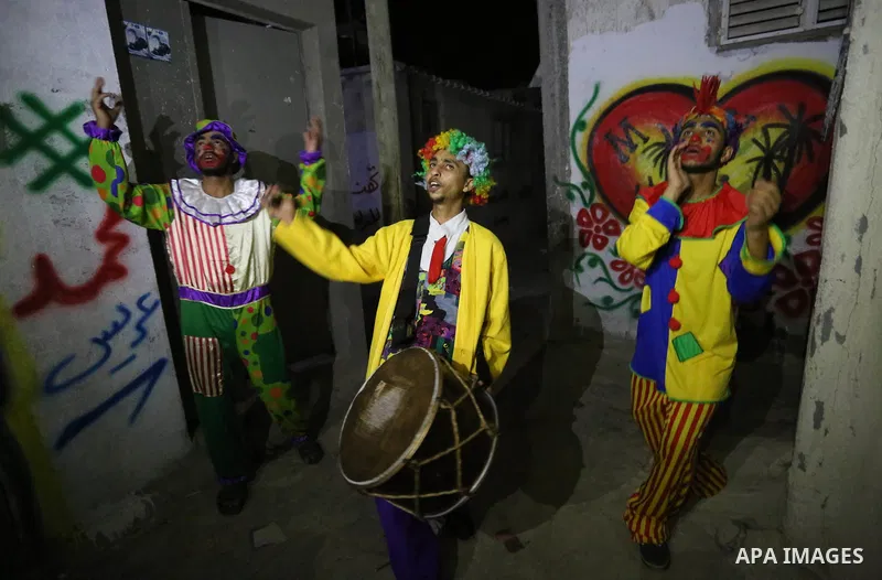 Palestinians dressed as clowns dawn awakener or Al Musaharati in Arabic, beat on their drums to wake Muslims for their overnight 'sahur', last meal, before the day's fast, as they walk through streets, in Dair Al Balah i...