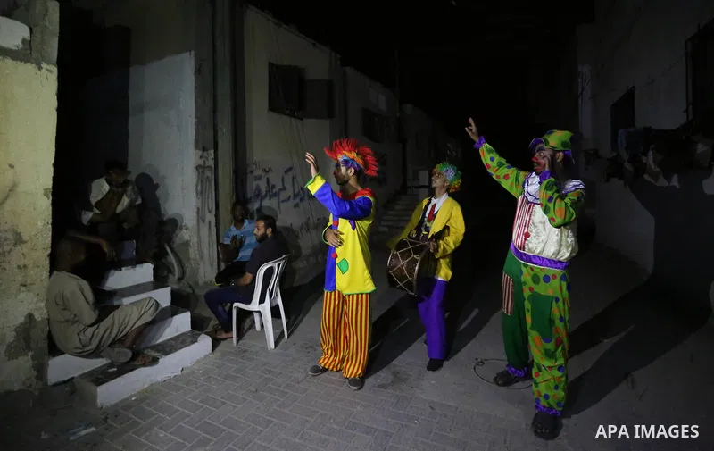 Palestinians dressed as clowns dawn awakener or Al Musaharati in Arabic, beat on their drums to wake Muslims for their overnight 'sahur', last meal, before the day's fast, as they walk through streets, in Dair Al Balah i...