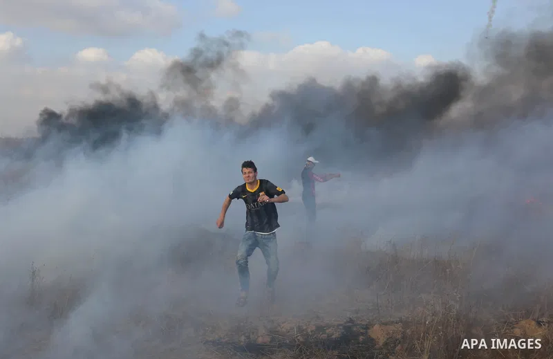 Palestinian protesters run for cover from tear gas canisters fired by Israeli security forces during clashes in a tent city protest where Palestinians demand the right to return to their homeland and against U.S. embassy...