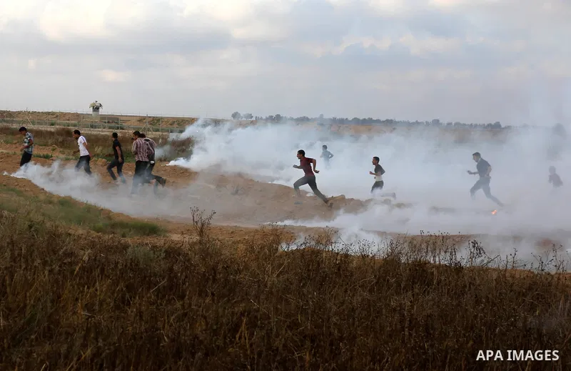 Palestinian protesters run for cover from tear gas canisters fired by Israeli security forces during clashes in a tent city protest where Palestinians demand the right to return to their homeland and against U.S. embassy...