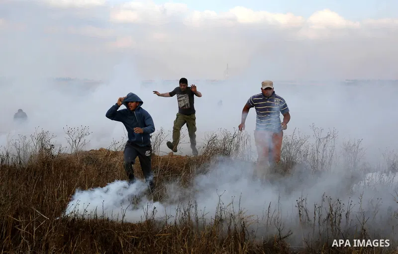 Palestinian protesters run for cover from tear gas canisters fired by Israeli security forces during clashes in a tent city protest where Palestinians demand the right to return to their homeland and against U.S. embassy...