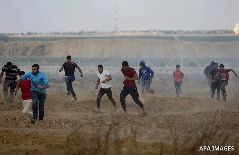 Palestinian protesters run for cover from tear gas canisters fired by Israeli security forces during clashes in a tent city protest where Palestinians demand the right to return to their homeland and against U.S. embassy...