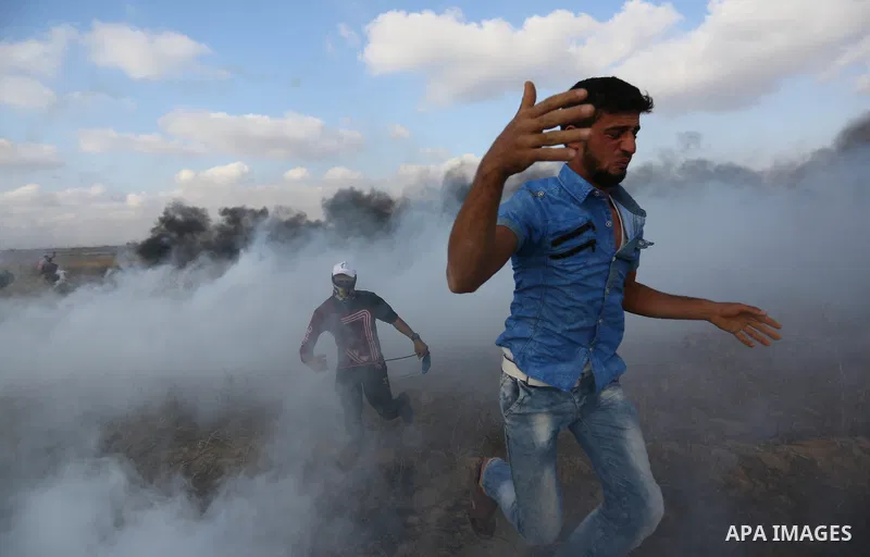 Palestinian protesters run for cover from tear gas canisters fired by Israeli security forces during clashes in a tent city protest where Palestinians demand the right to return to their homeland and against U.S. embassy...