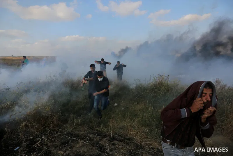 Palestinian protesters run for cover from tear gas canisters fired by Israeli security forces during clashes in a tent city protest where Palestinians demand the right to return to their homeland and against U.S. embassy...