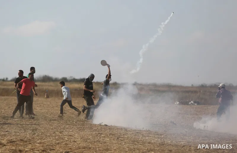 Palestinian protesters run for cover from tear gas canisters fired by Israeli security forces during clashes in a tent city protest where Palestinians demand the right to return to their homeland and against U.S. embassy...