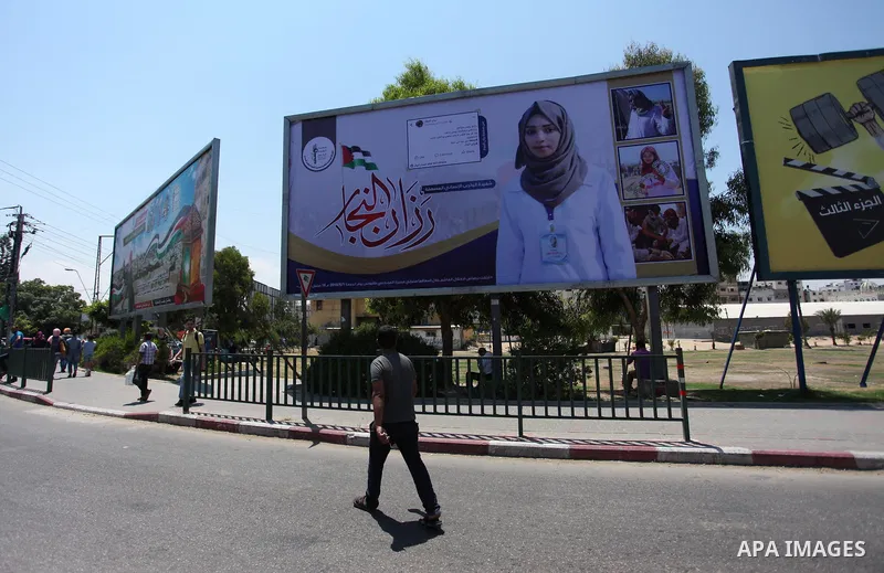 Palestinians walk past a mural depicting nurse Razan Al-Najar, who was shot dead by Israeli soldiers, during a protest at the Israel-Gaza border, in Gaza City on June 4, 2018. Razan Al-Najar’s death brought to 119 the nu...