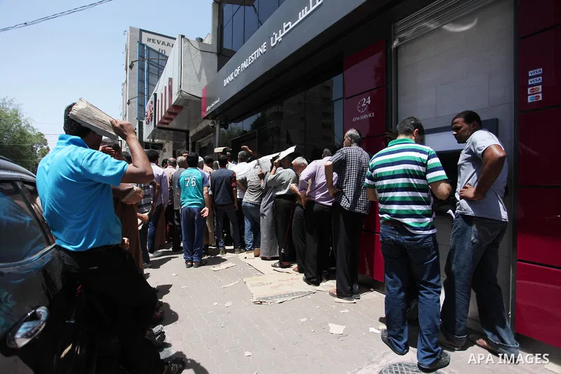 Palestinians of Social Affairs wait in front of Bank of Palestine to withdraw their financial aid in Gaza City on June 10, 2018. Photo by Mahmoud Ajour
