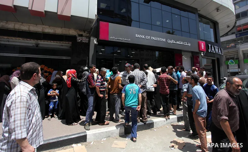 Palestinians of Social Affairs wait in front of Bank of Palestine to withdraw their financial aid in Gaza City on June 10, 2018. Photo by Mahmoud Ajour