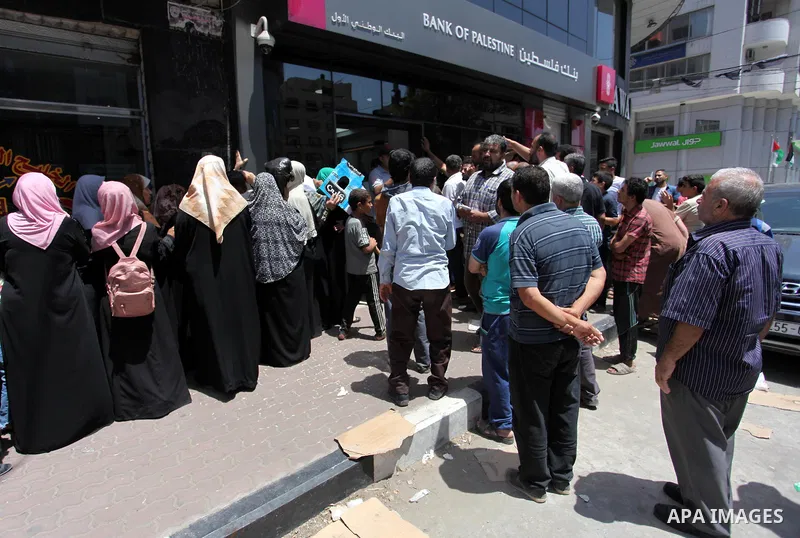 Palestinians of Social Affairs wait in front of Bank of Palestine to withdraw their financial aid in Gaza City on June 10, 2018. Photo by Mahmoud Ajour